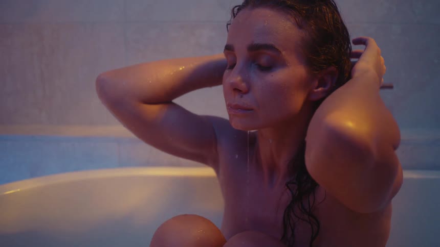 A woman sits in a bathtub and pours water over hear own head with her hands
