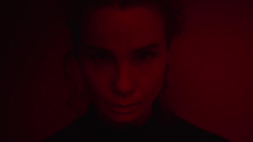 A woman bathed in a red glowing light breathes heavily while staring ahead