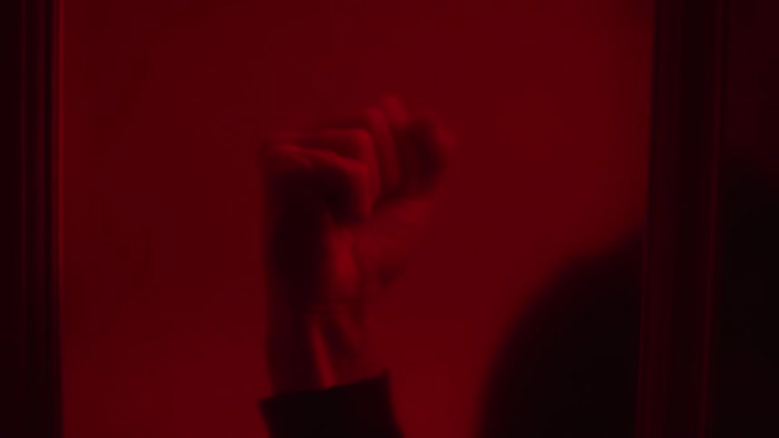 A fist pounding against glass in a reddish glow