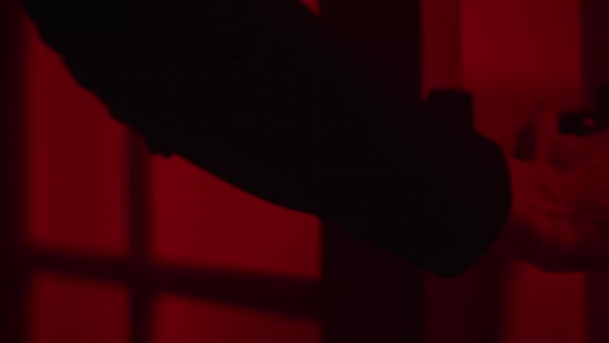A womans hand grasps the latch of a door and when she tries to open the door someone is pulling from the other side