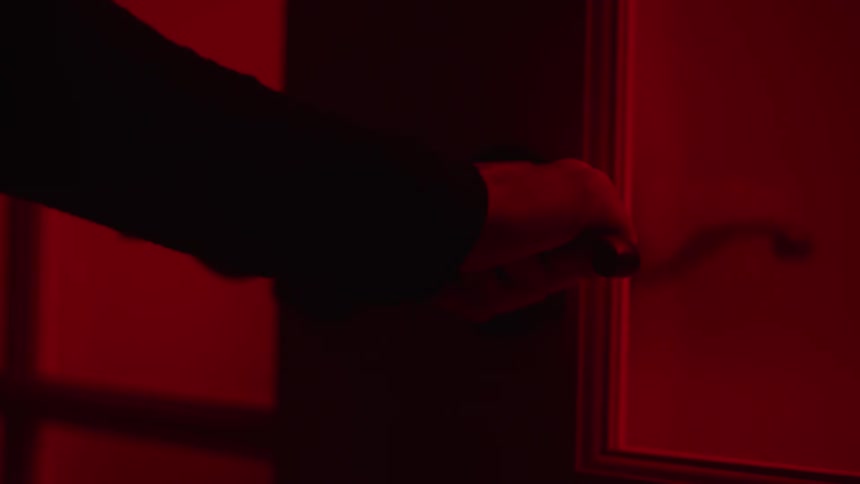 A womans hand grasps the latch of a door with red light on the other side and the door will not open