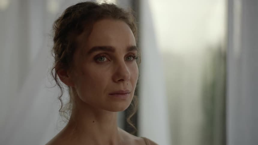 A woman standing in front of a window turns her head