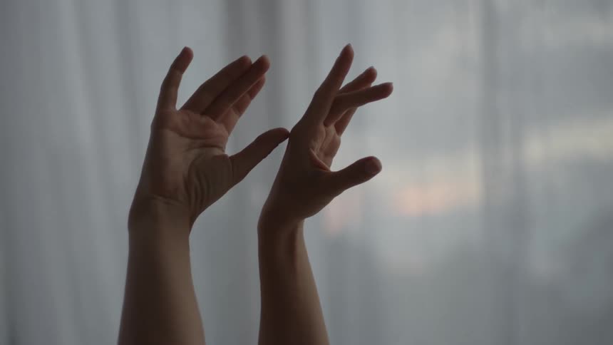 A womans hands and fingers are in motion as she raises her arms in the air