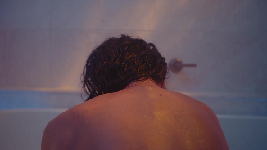 A person is sitting in a bathtub and is facing the wall