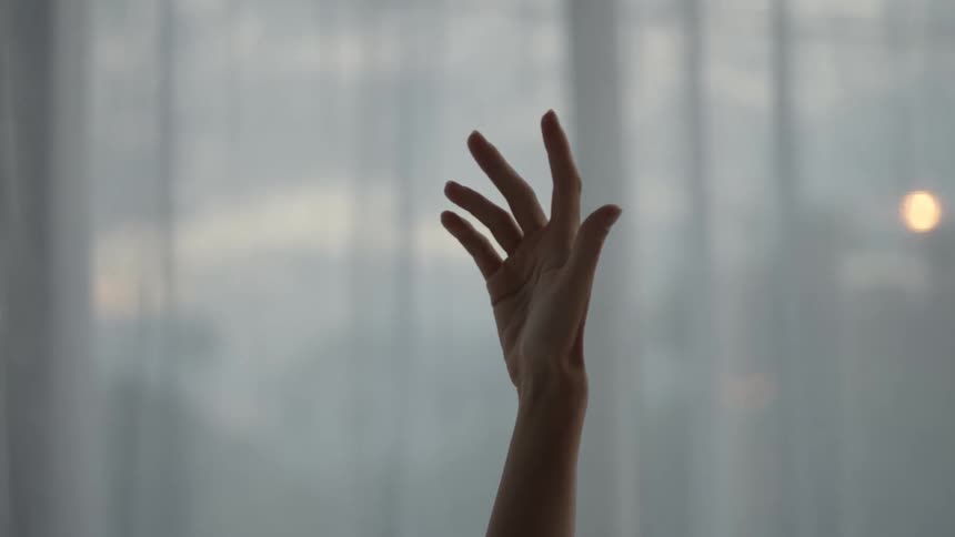 A woman waves her hand around in front of a window