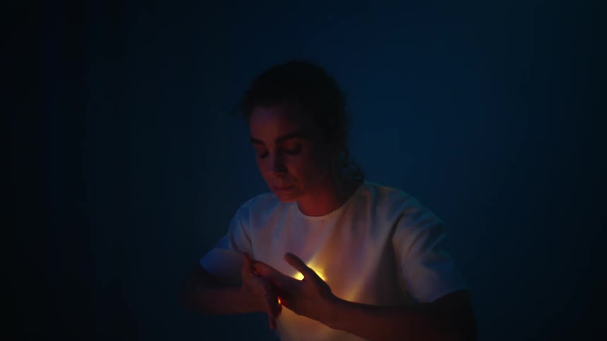 A woman holds her hands in front of a light that is emitting from the center of her chest