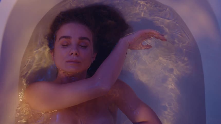 A woman floating in her bath tub pushing off the side relaxing with shimmering lights