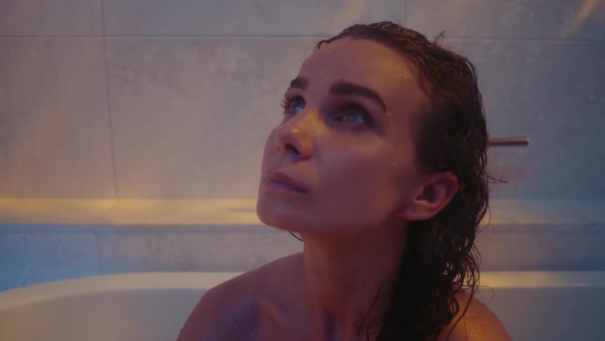 A woman is sitting in a bathtub and looking at the ceiling