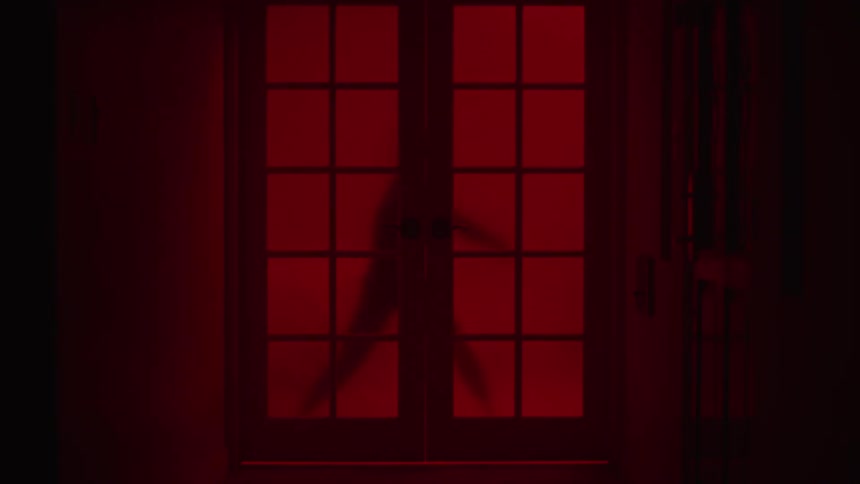 The silhouette of a woman vigorously dancing can be seen through red curtains over windows