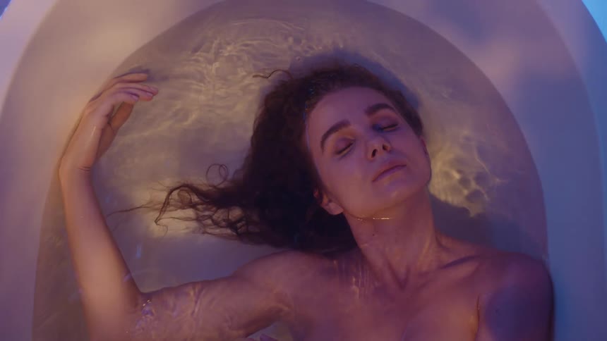 A woman lying in a bathtub of water moves her head from side to side