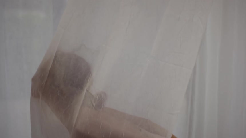 Woman dancing slowly under translucent curtains near a window at evening