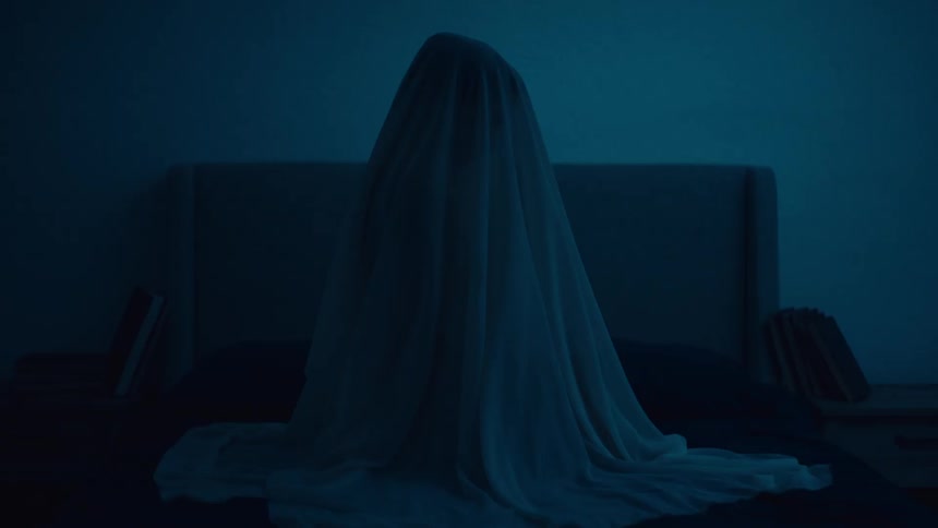 A woman sits under a sheer cloth in bed with a tablet