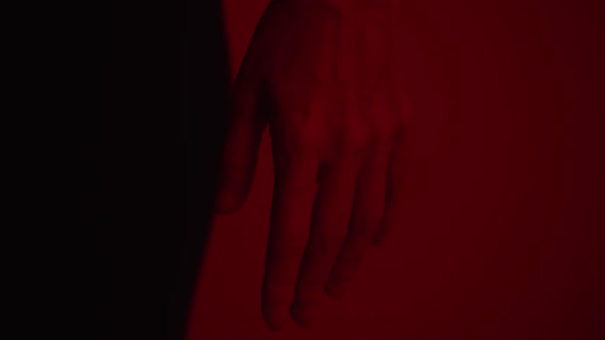 A person standing tightly squeezes their hand closed into a first