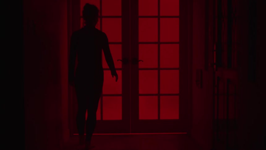 The silhouette of a woman walking to a door with red curtains over the windows