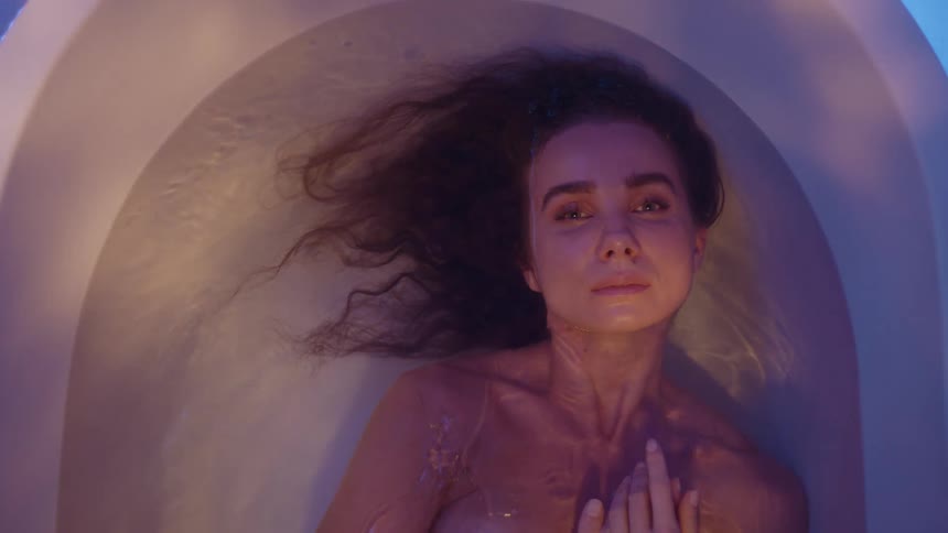 A woman is lying in a bathtub on her back moving back and forth with her face just above the water