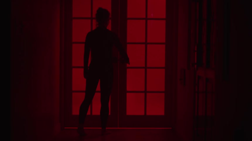 The silhouette of a woman approaching red glowing french doors then struggling to keep it closed