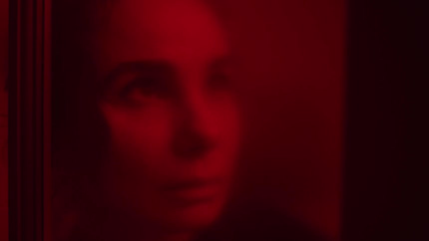 A woman looking through a window with a red hue