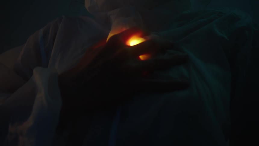 A person grasps at a pulsating yellow light under the shirt on their chest