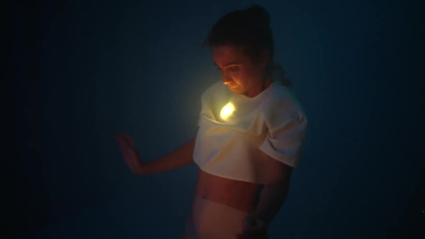 A dancer with a glowing light under her shirt performs emotionally