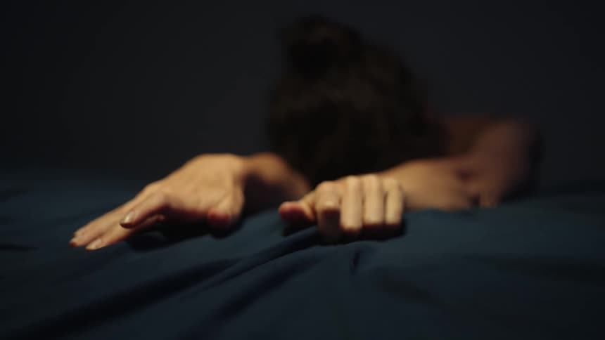 Woman leans against bed her hands grasping the covers