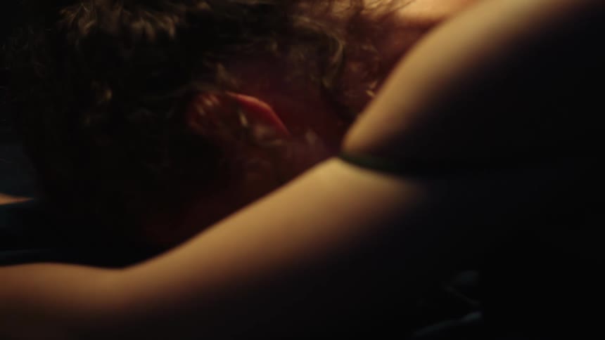 Woman lying facedown on bed grasps and strokes the covers