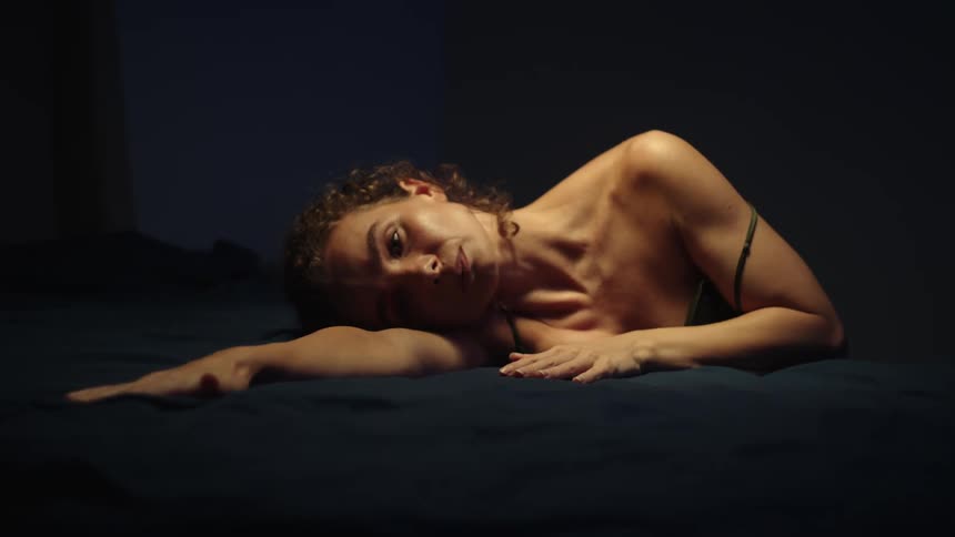 A woman sits with her head facing down onto her bed