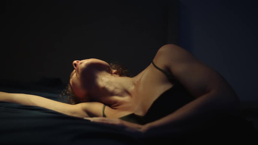 There is a young white woman laying in bed and moving around