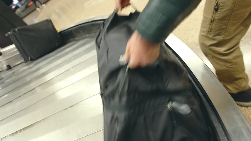A man lifting a black duffel back from a rotating baggage claim
