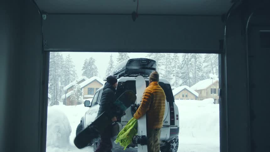 Two men load snowboards into their vehicle in the driveway