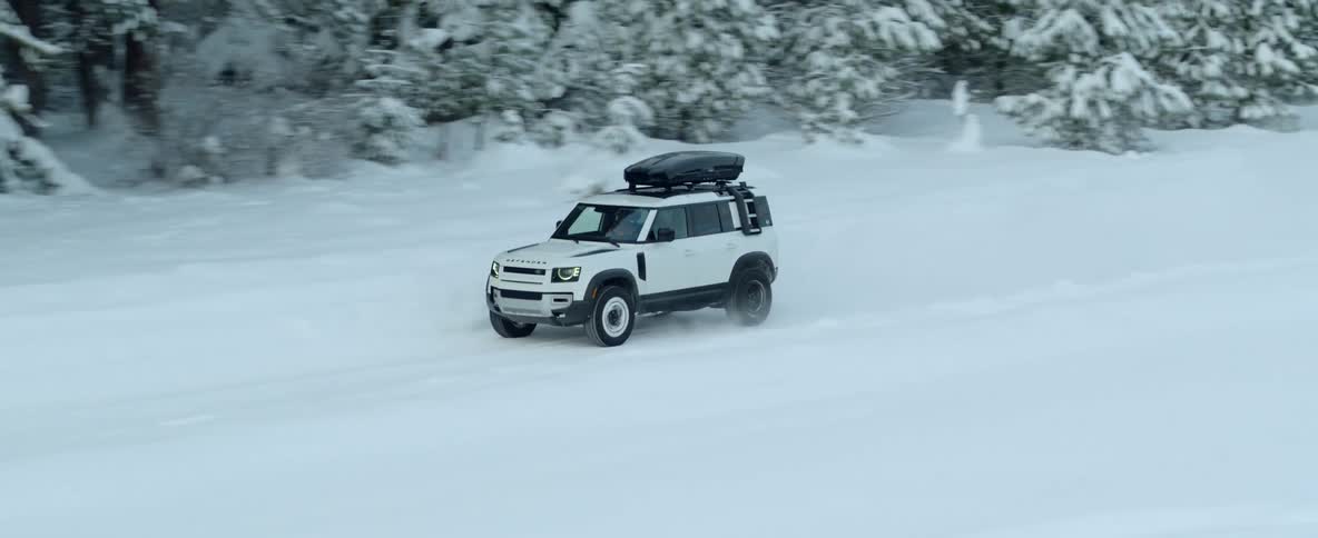 An automobile is traveling on a snow covered road through a rural forested area on a winter day
