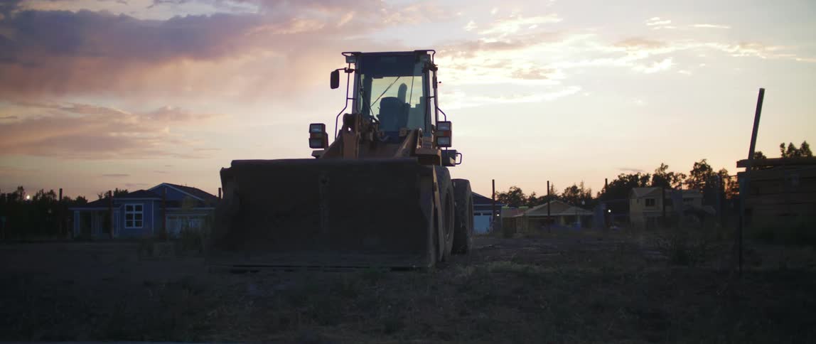 A bulldozer sitting in a lot next to lumber piles in an unfinished subdivision