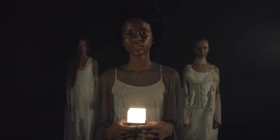 A woman holding an illuminated cube is flanked by two other women