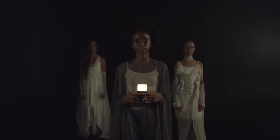 A young model holds a flash while standing in front of two women