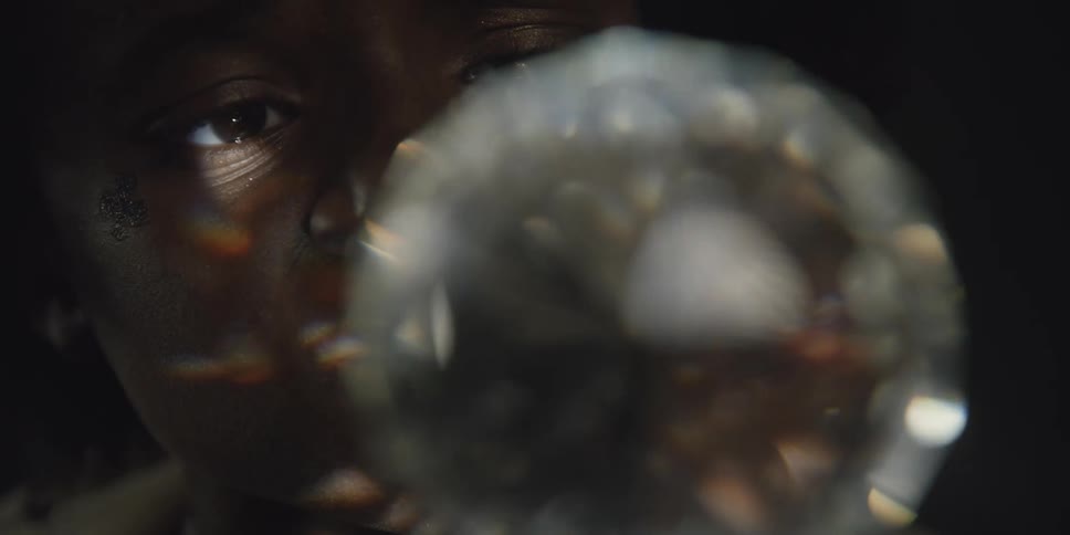 Light reflects on the face of a woman from a rotating multifaceted cut glass globe in a dark room