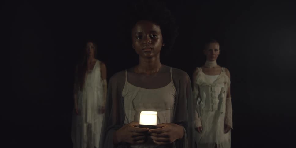 Three woman stand in a group forming a triangle as the one in front holds a light
