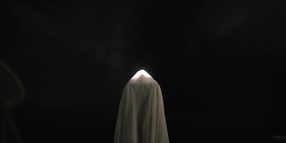 Surreal footage of a girl slowly walking towards what appears to be a figure under a white sheet