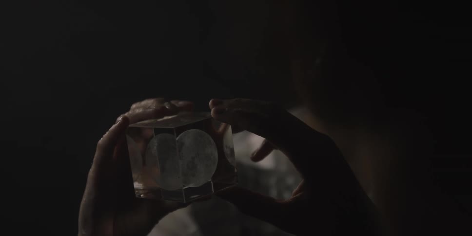 A woman stands holding a glass cube with shapes etched on it