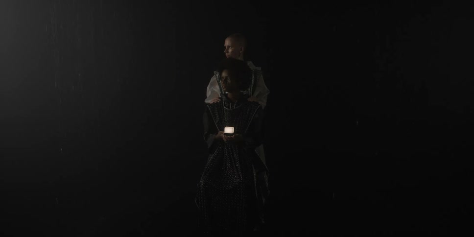 Two women pose in the darkness with one in front of the other