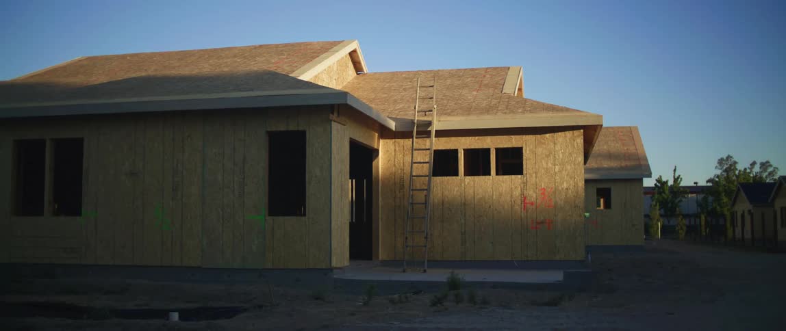 Sunlight shines on buildings being constructed and a ladder rests against the roof