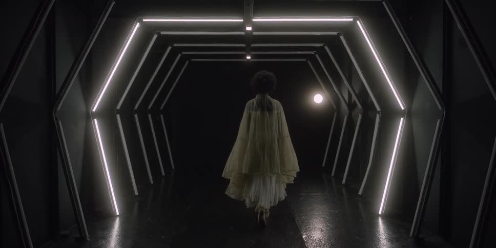 Section lights turn on as a woman walks down a corridor wearing a long sheer gown