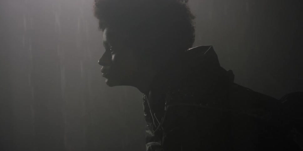 A woman sitting in the rain lifts her head in profile