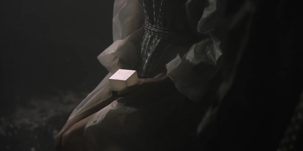 A woman sits in the dark next to a river holding a small box