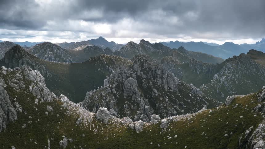 Light reflects on mountains as the clouds move across the sky and silhouettes of mountains are on the horizon