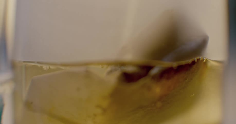 Boiling water is poured into a clear glass cup with a tea bag inside