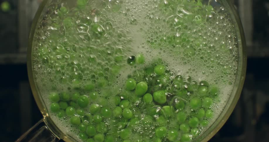 Flame shines through bottom of glass pot after person wearing oven glove removes lid to show boiling peas