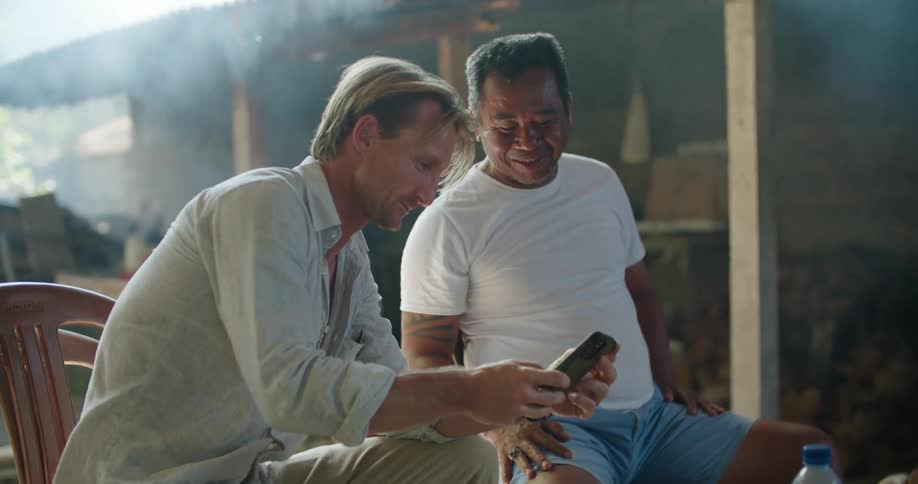 Smoke and steam billow out from a shack workshop while two men look at photos on a phone