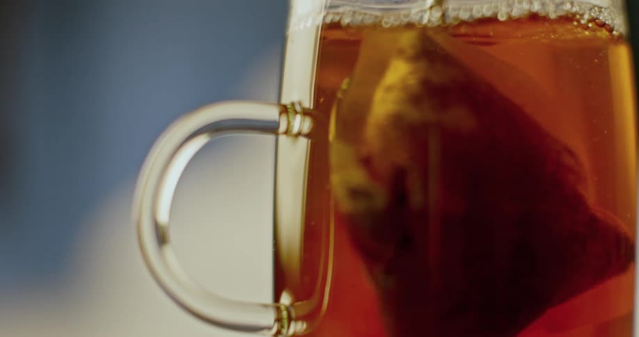 A spoon plunges into a glass cup and stirs a tea bag around