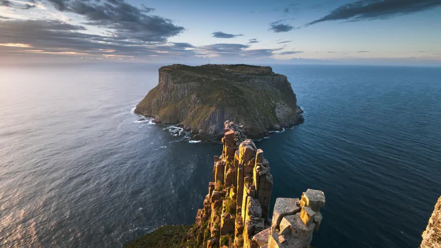 Clouds move over an island near a tall rock formation as the water ripples and waves