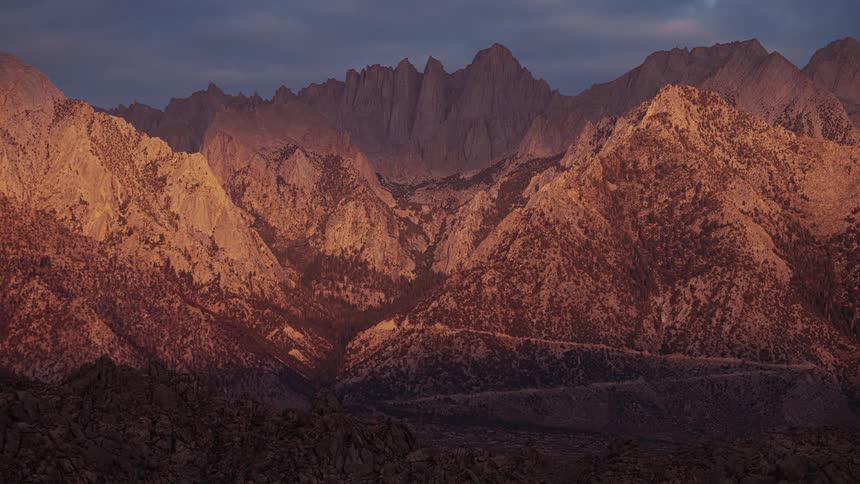 Shadows begin to cover a jagged mountain range as the sun is setting