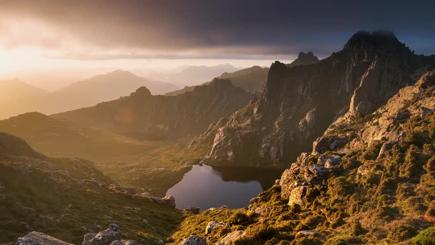 A time lapse of clouds and sun shining golden light over lake and mountains